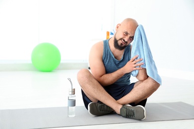 Tired overweight man wiping sweat off forehead in gym