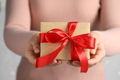 Photo of Woman holding gift box with red bow on light grey background, closeup