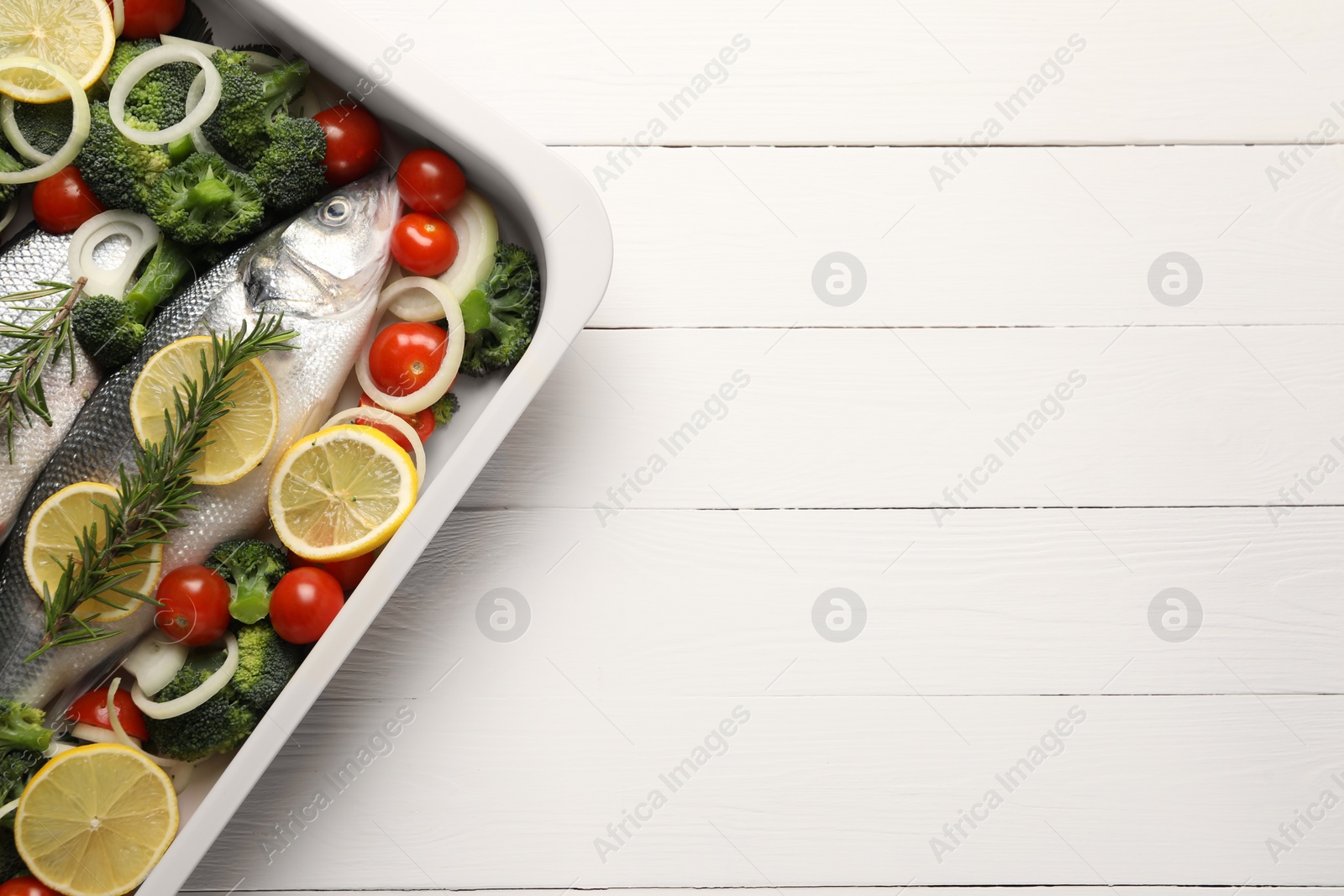 Photo of Raw fish with vegetables and lemon in baking dish on white wooden table, top view. Space for text