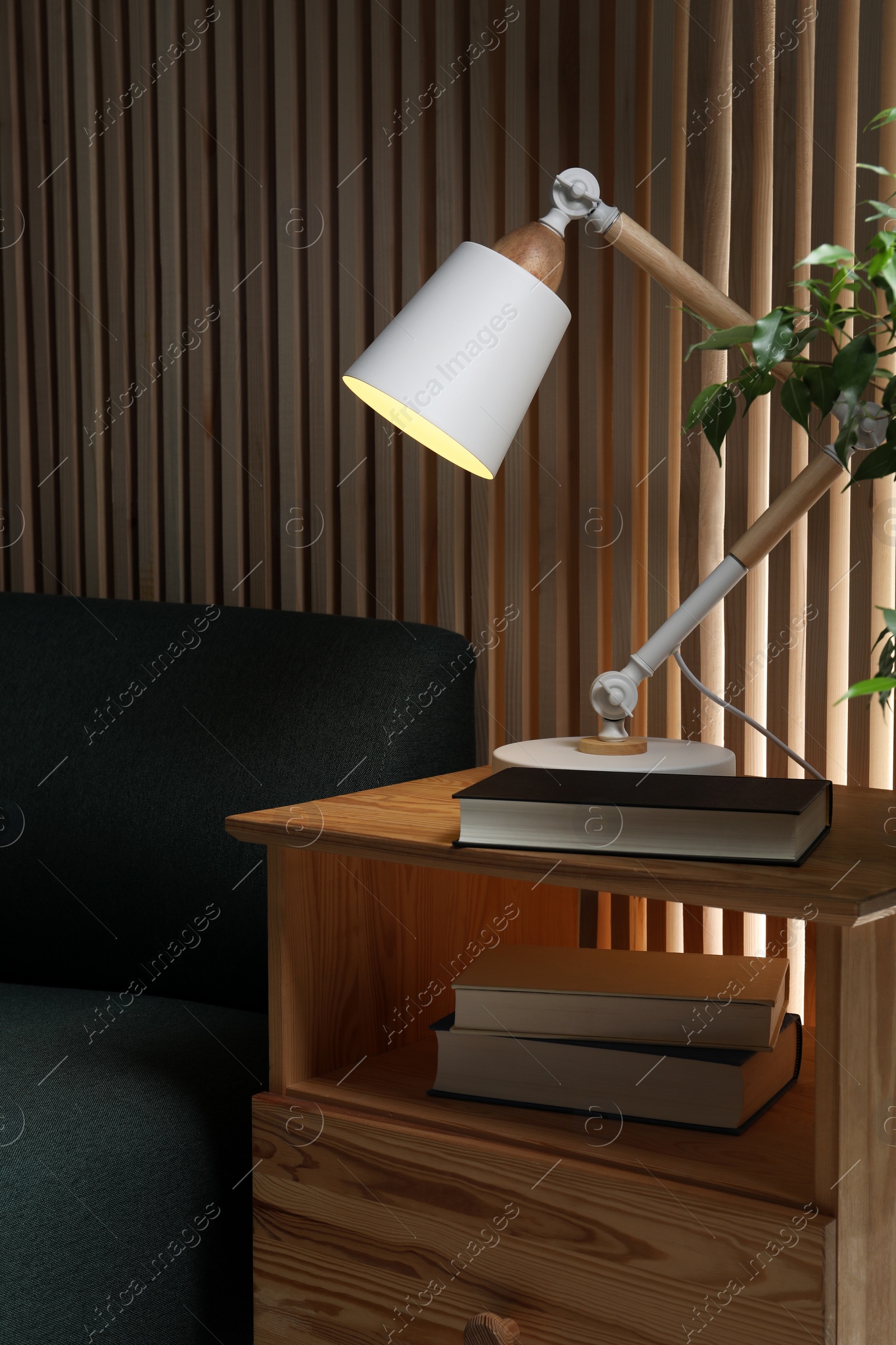 Photo of Stylish modern desk lamp and book on wooden cabinet in living room