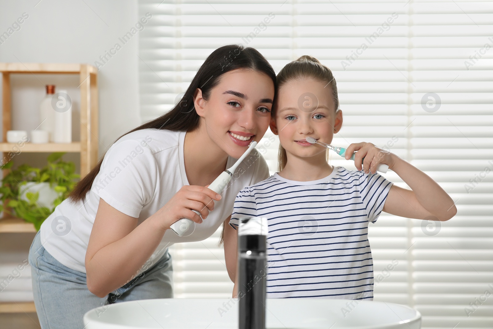 Photo of Mother and her daughter brushing teeth together in bathroom