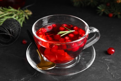 Photo of Tasty hot cranberry tea with rosemary and lemon on black table