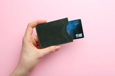 Photo of Woman holding leather card holder with credit card on pink background, top view