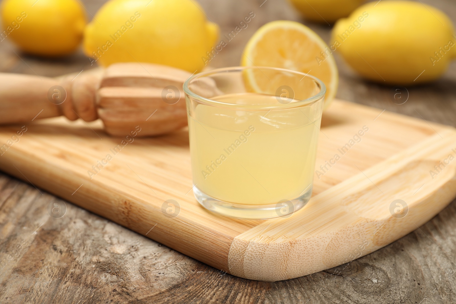 Photo of Wooden board with glass of freshly squeezed lemon juice and reamer on table