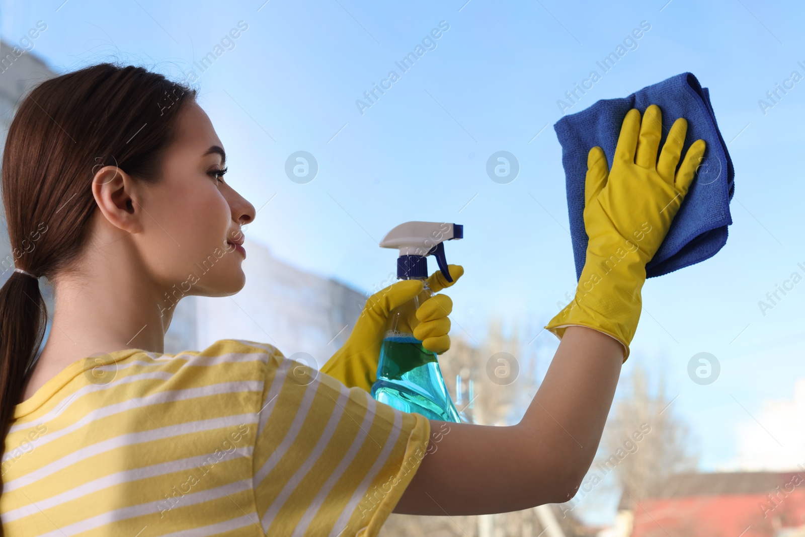 Photo of Young woman cleaning window glass with rag and detergent