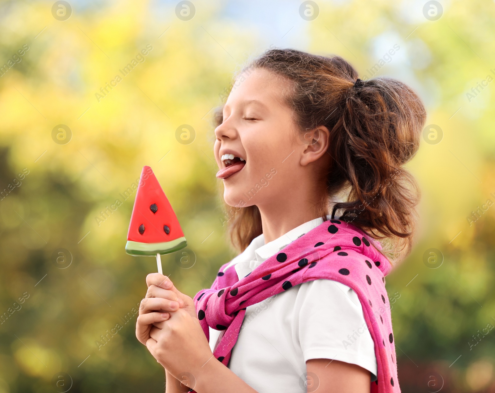 Photo of Cute little girl with tasty candy outdoors