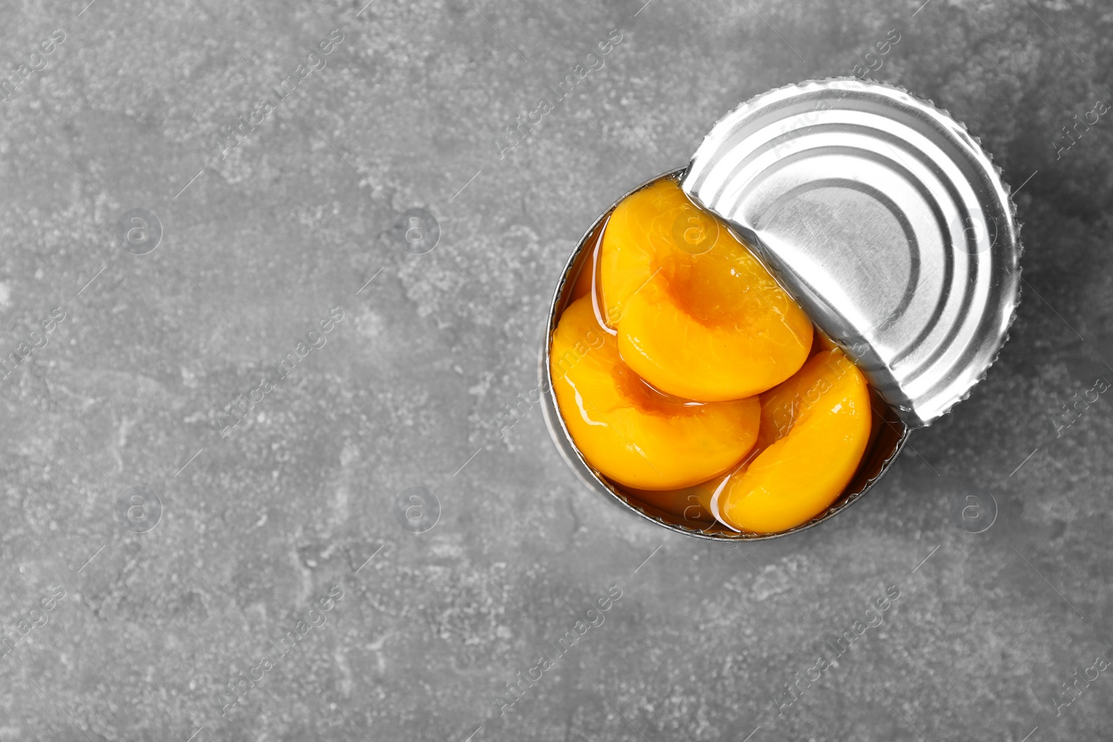 Photo of Tin can with conserved peaches on grey background, top view