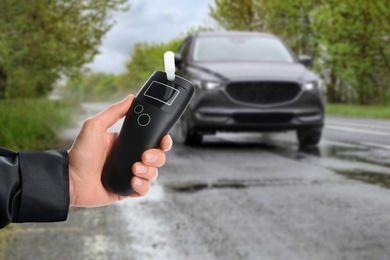 Image of Police officer with breathalyzer and car on road. Alcohol consumption while driving