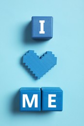 Photo of Phrase I Love Me made with wooden cubes and heart on light blue background, flat lay