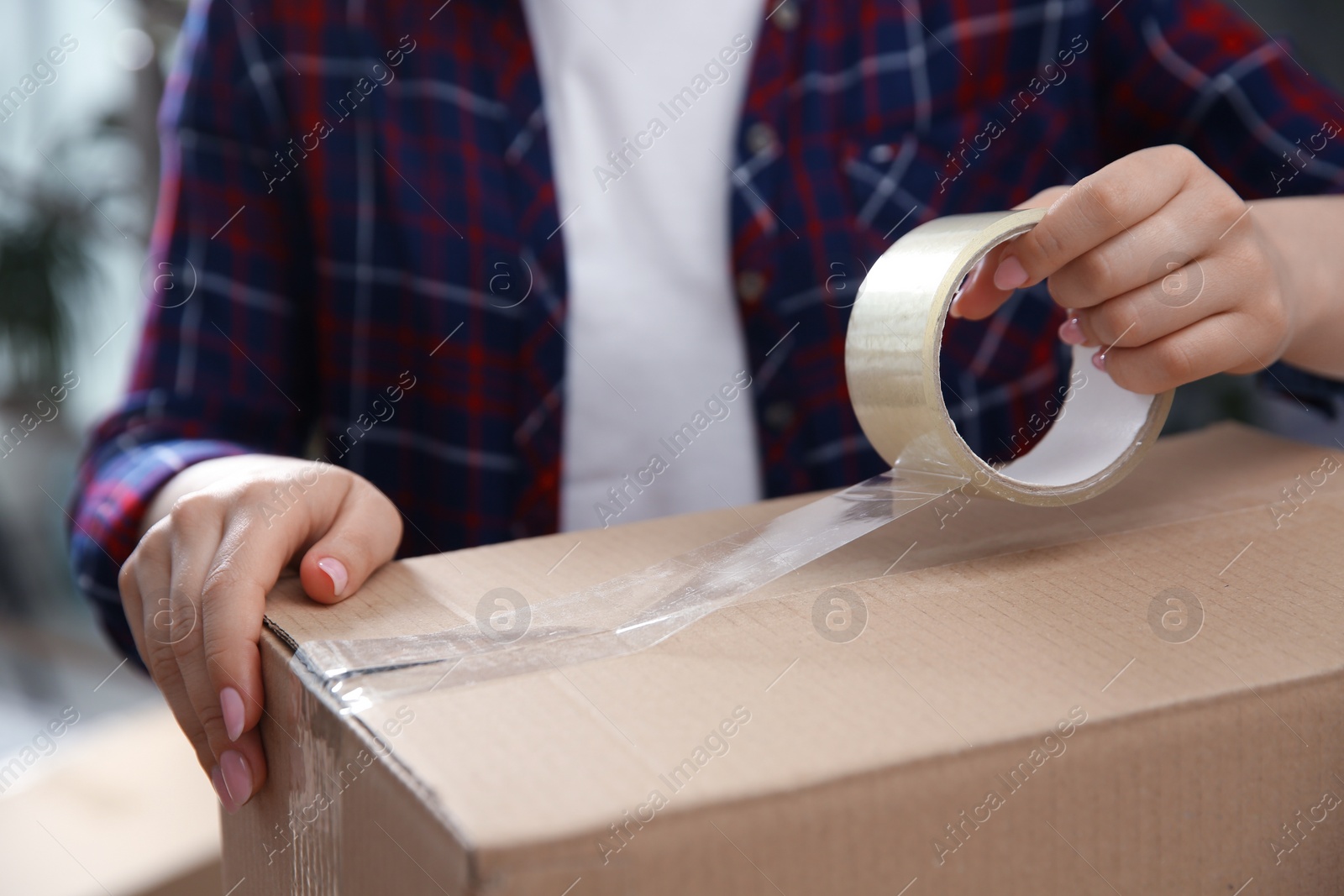 Photo of Woman taping cardboard box indoors, closeup. Moving day