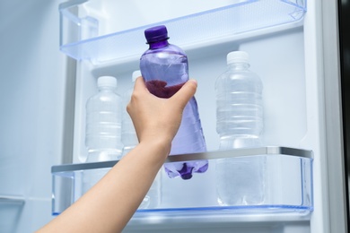 Woman taking bottle of water from refrigerator, closeup