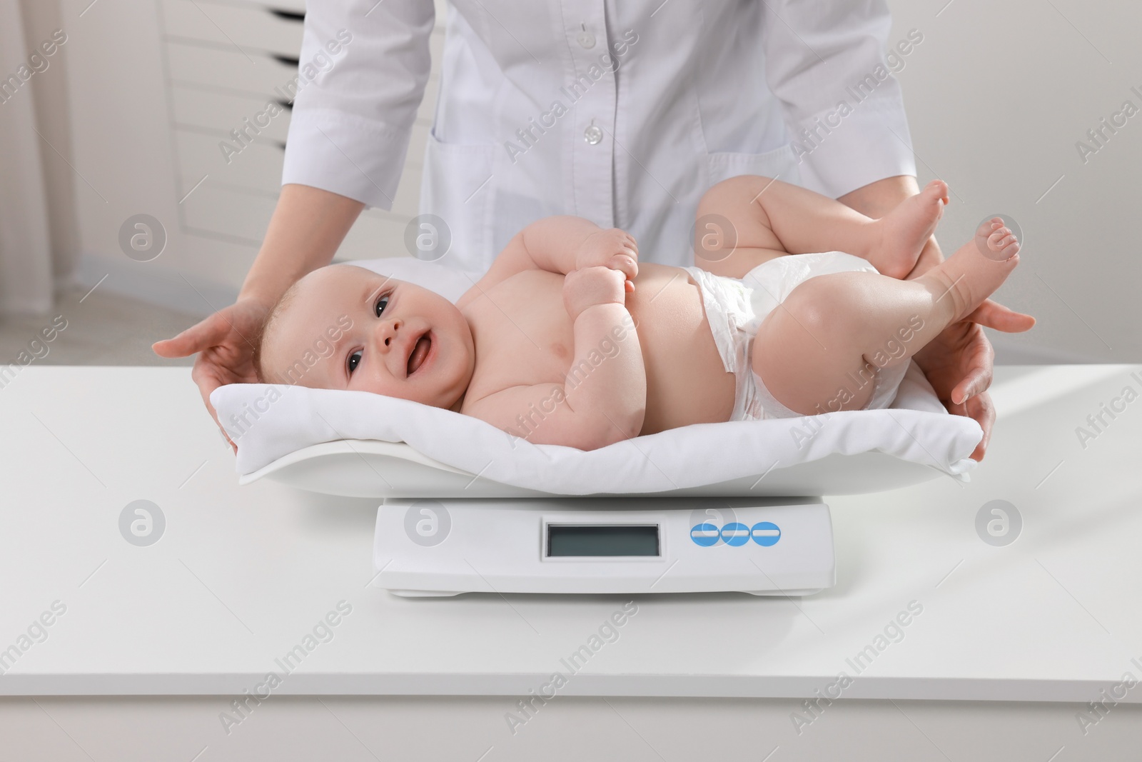 Photo of Pediatrician weighting cute little baby in clinic, closeup