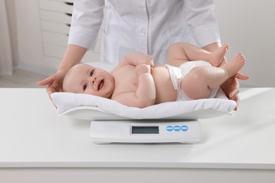 Pediatrician weighting cute little baby in clinic, closeup