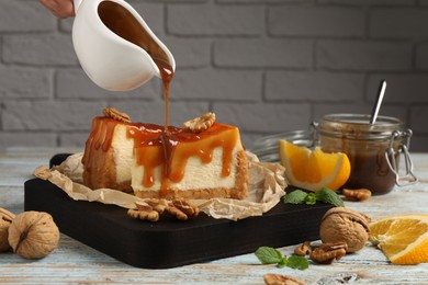 Woman pouring caramel sauce onto delicious pieces of cheesecake at wooden table, closeup