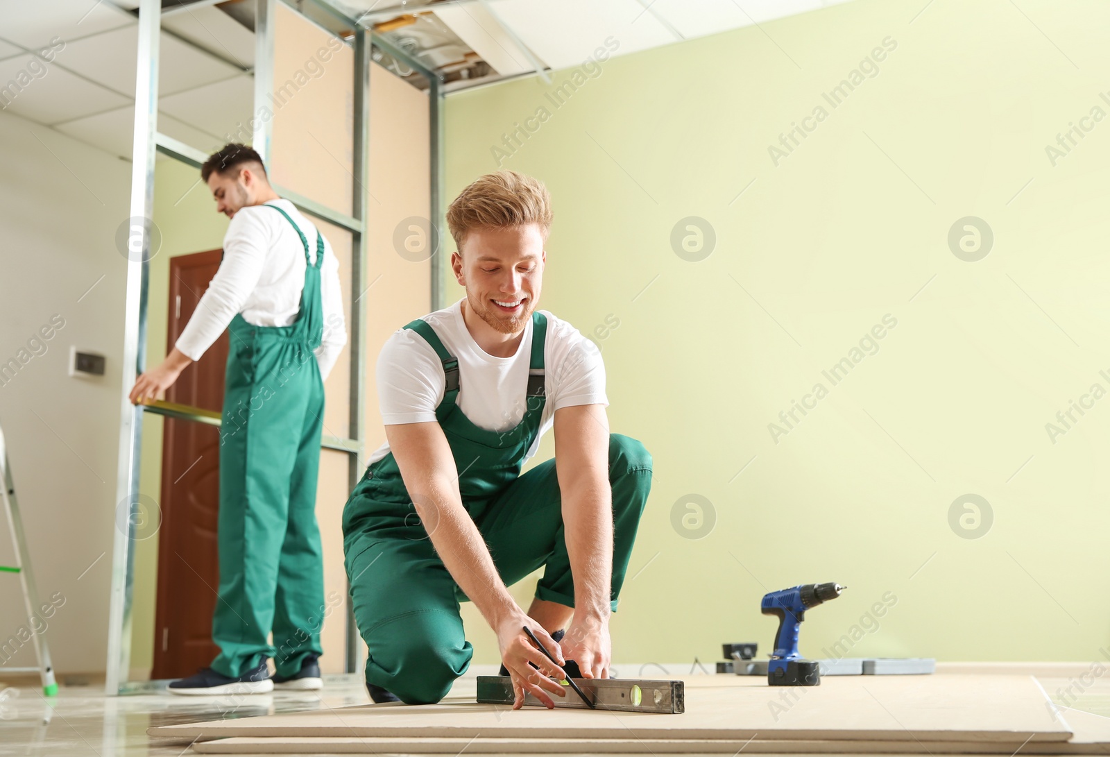 Photo of Young workers installing drywall indoors. Home repair service