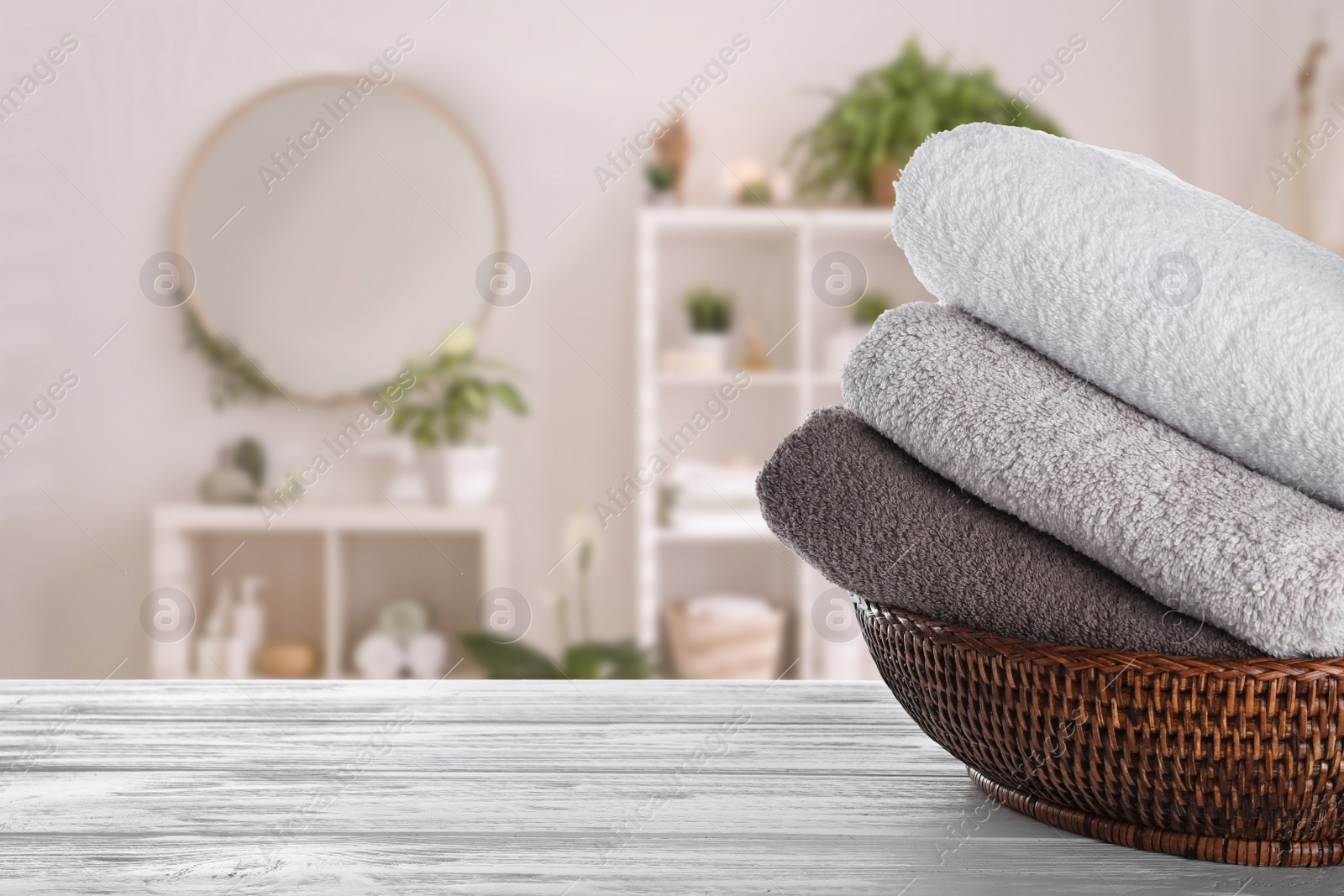 Image of Wicker basket with clean soft towels on white wooden table in bathroom. Space for text