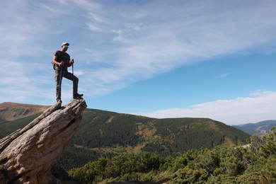 Photo of Man with backpack and trekking poles on rocky peak in mountains