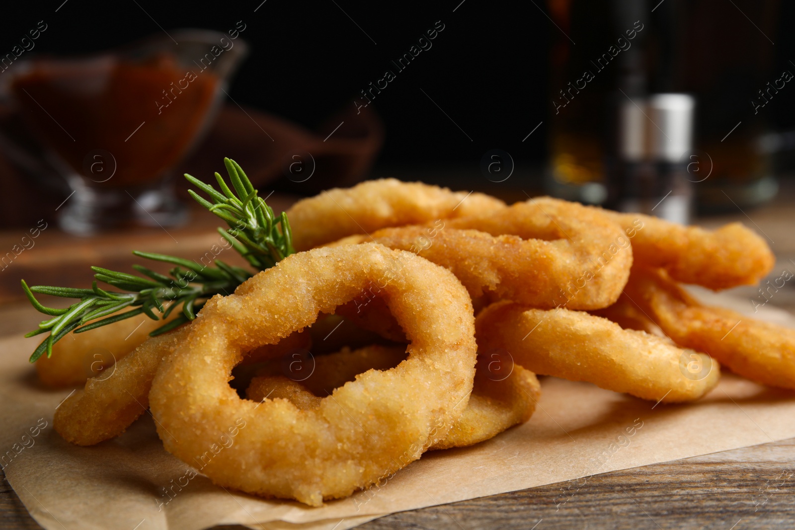 Photo of Pile of delicious crunchy fried onion rings with rosemary on wooden table, closeup