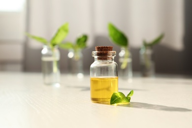 Photo of Bottle of essential basil oil on table against blurred background