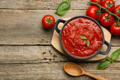 Photo of Homemade tomato sauce in bowl, spoon and fresh ingredients on wooden table, flat lay. Space for text