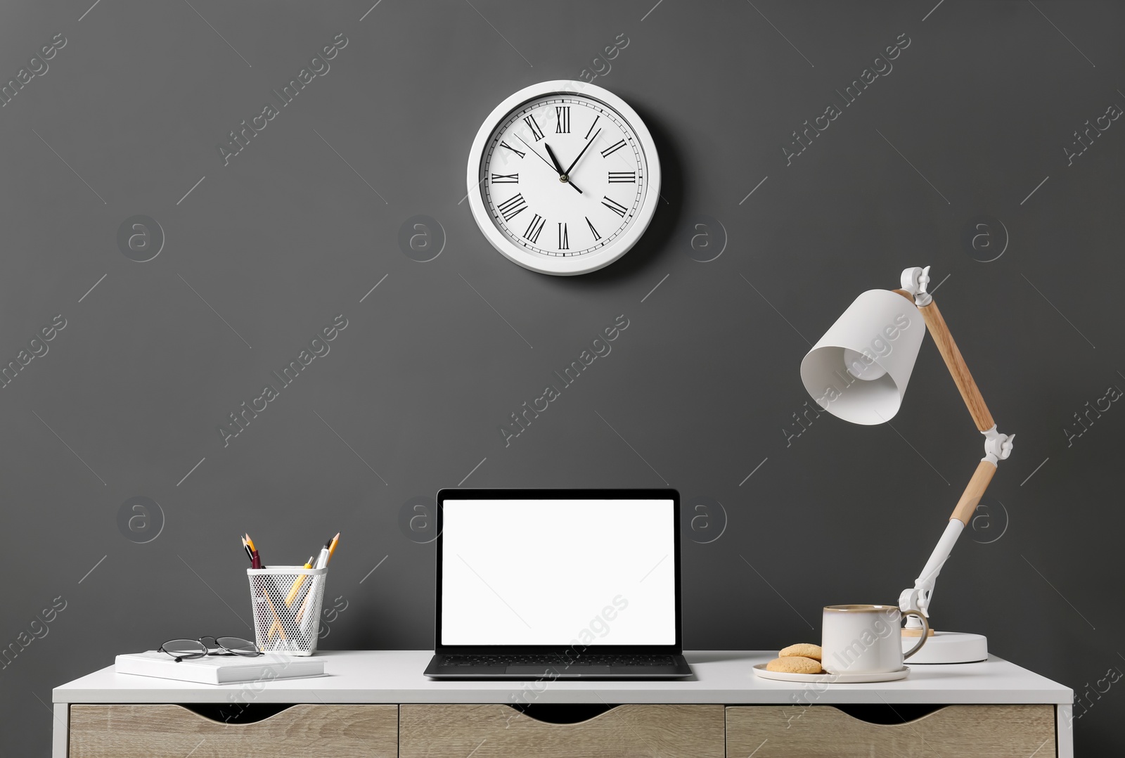 Photo of Stylish workplace with laptop, lamp and stationery on white table near grey wall