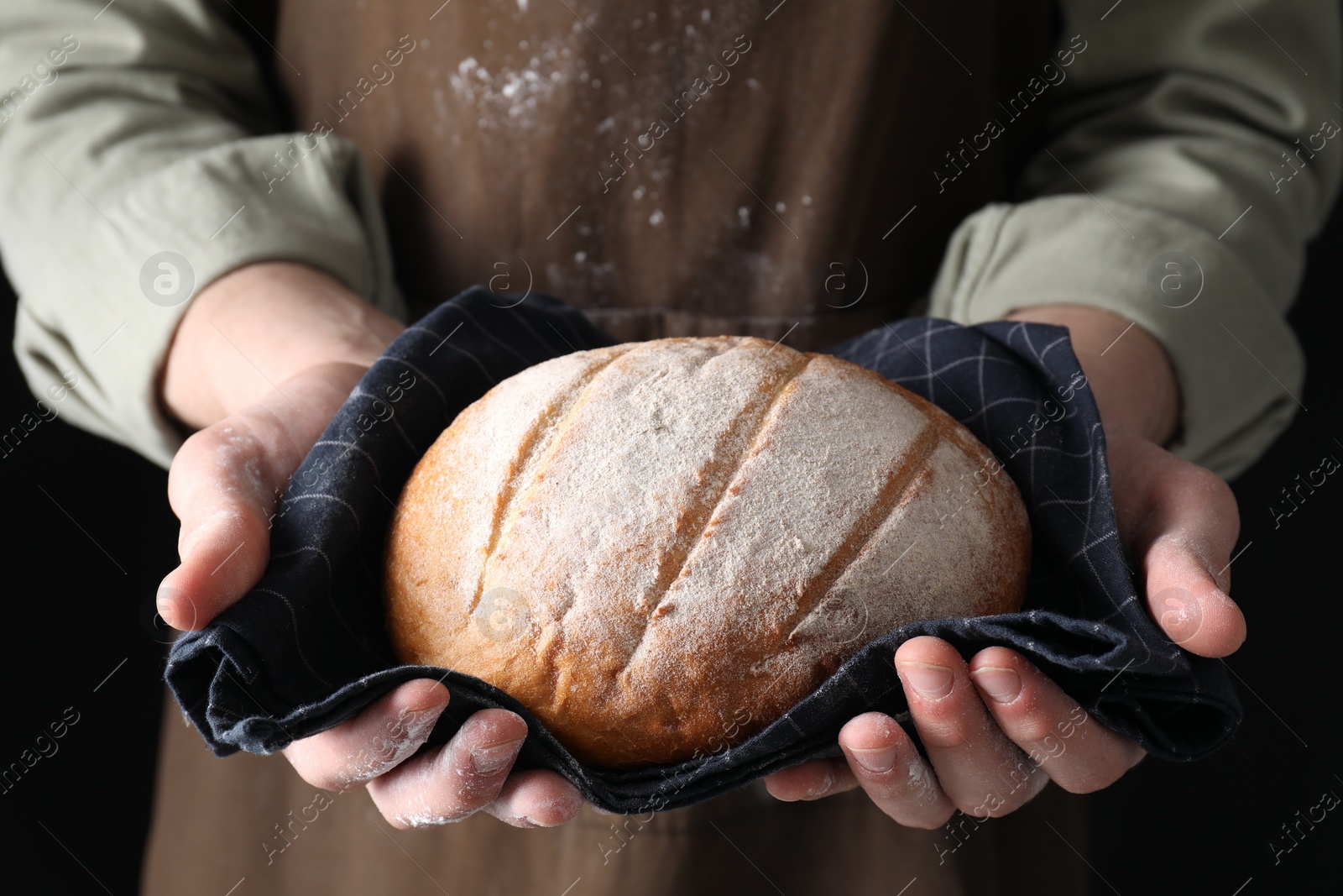 Photo of Woman holding freshly baked bread on black background, closeup