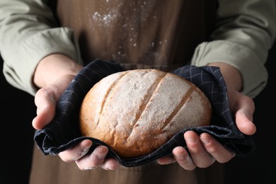 Woman holding freshly baked bread on black background, closeup