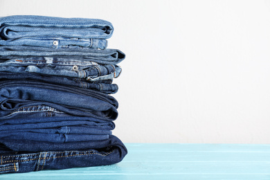 Photo of Stack of different jeans on blue wooden table. Space for text