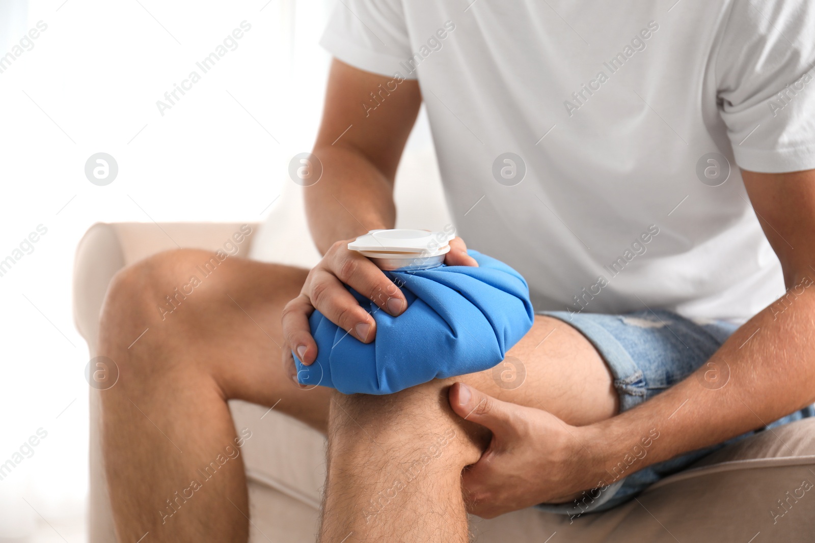 Photo of Man applying ice pack on knee at home, closeup. Health problems