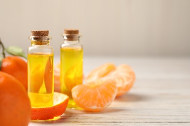 Bottles of tangerine essential oil, fresh fruits and peel on white wooden table, closeup. Space for text