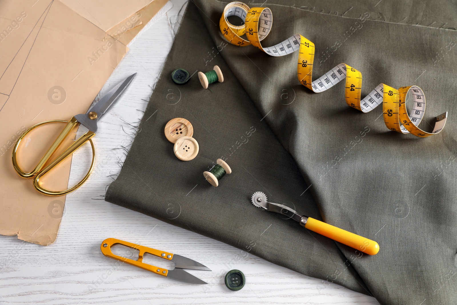 Photo of Set of sewing supplies and accessories with fabric on white wooden table, above view