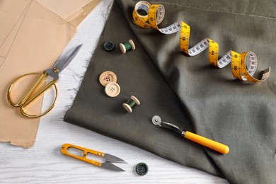 Photo of Set of sewing supplies and accessories with fabric on white wooden table, above view