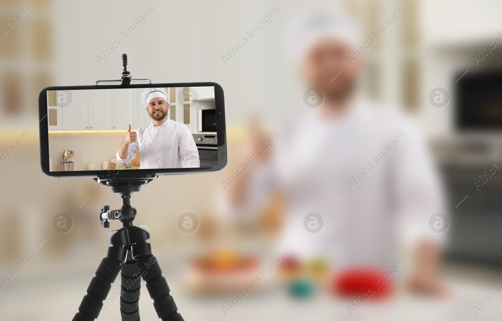 Image of Cook showing thumb up gesture in kitchen, selective focus on smartphone display