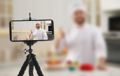 Cook showing thumb up gesture in kitchen, selective focus on smartphone display