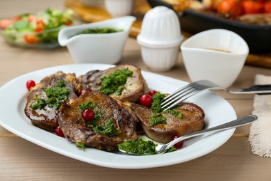 Photo of Tasty beef tongue pieces, salsa verde and berries on beige wooden table, closeup