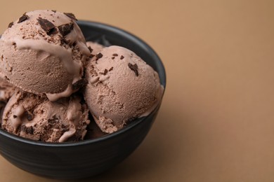 Bowl with tasty chocolate ice cream on light brown background, closeup. Space for text