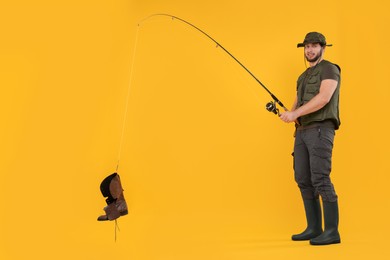 Photo of Fisherman with fishing rod and old boot on yellow background, space for text
