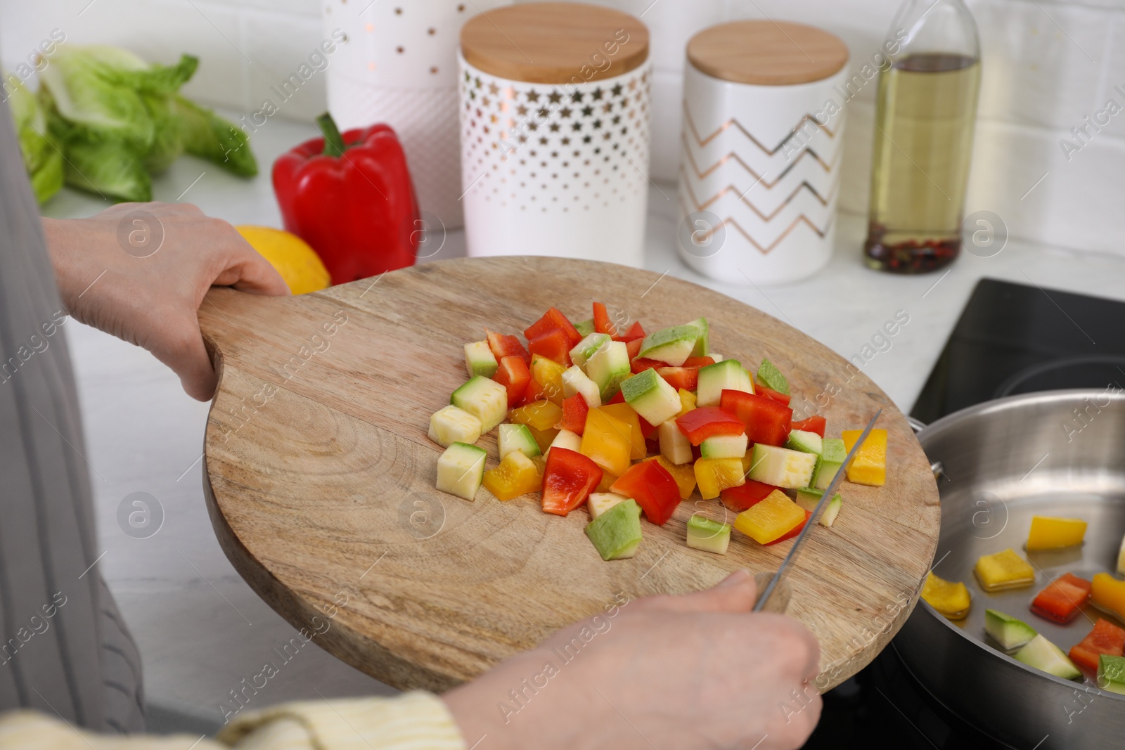 Photo of Woman putting cut vegetables into saute pan in kitchen, closeup