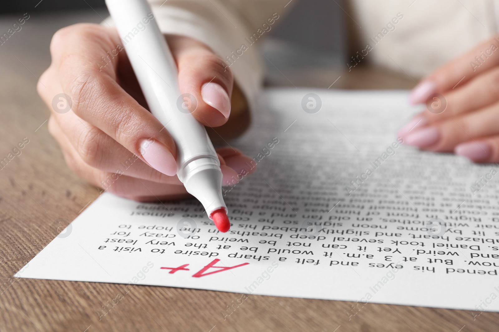 Photo of School grade. Teacher writing letter A with plus symbol on sheet of paper at wooden table, closeup