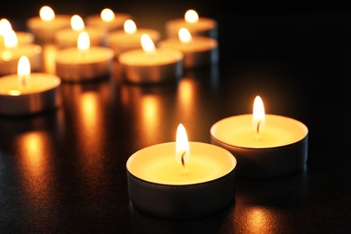 Photo of Wax candles burning on table in darkness, closeup