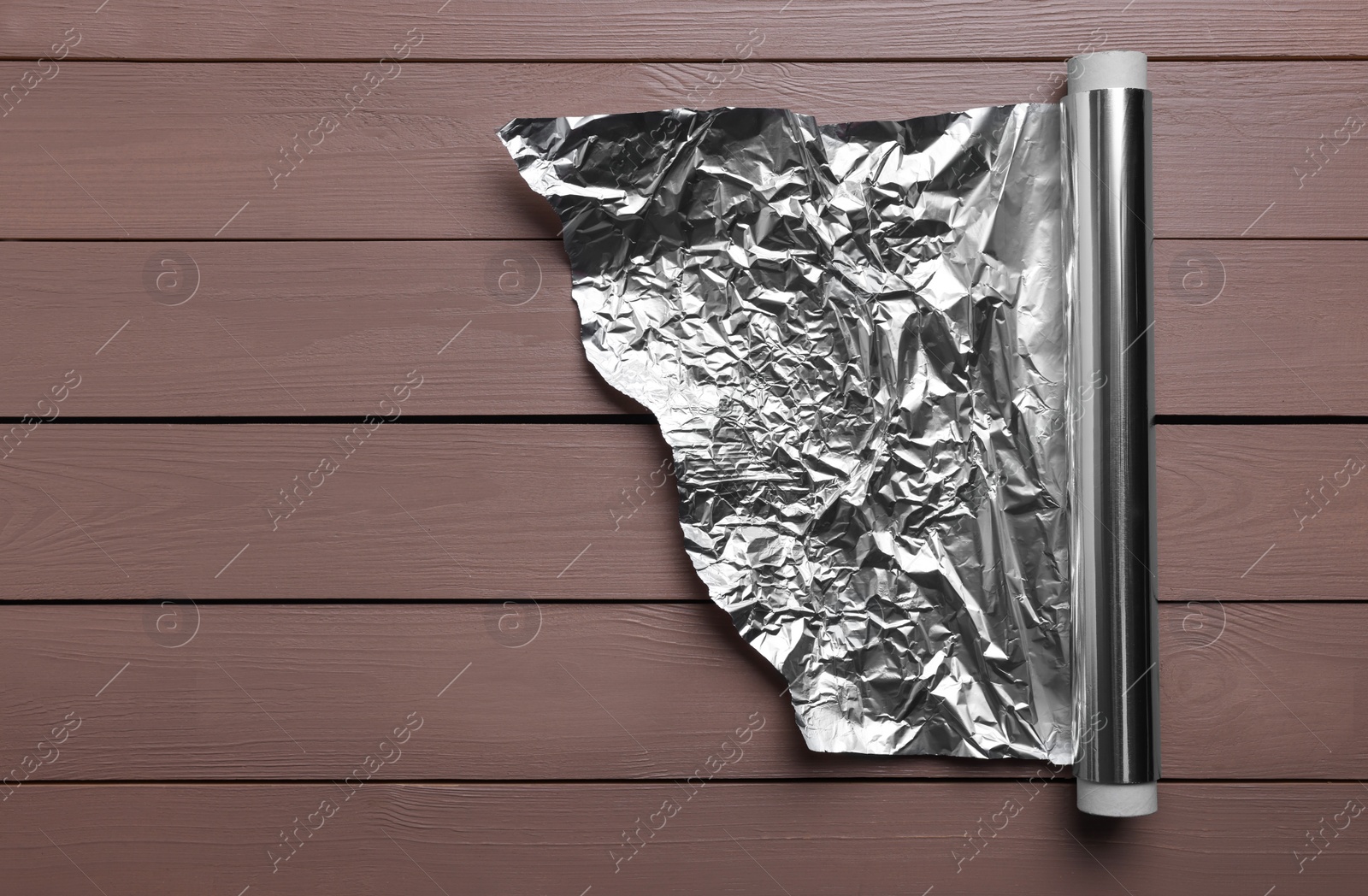 Photo of Roll of aluminum foil on wooden table, top view. Space for text