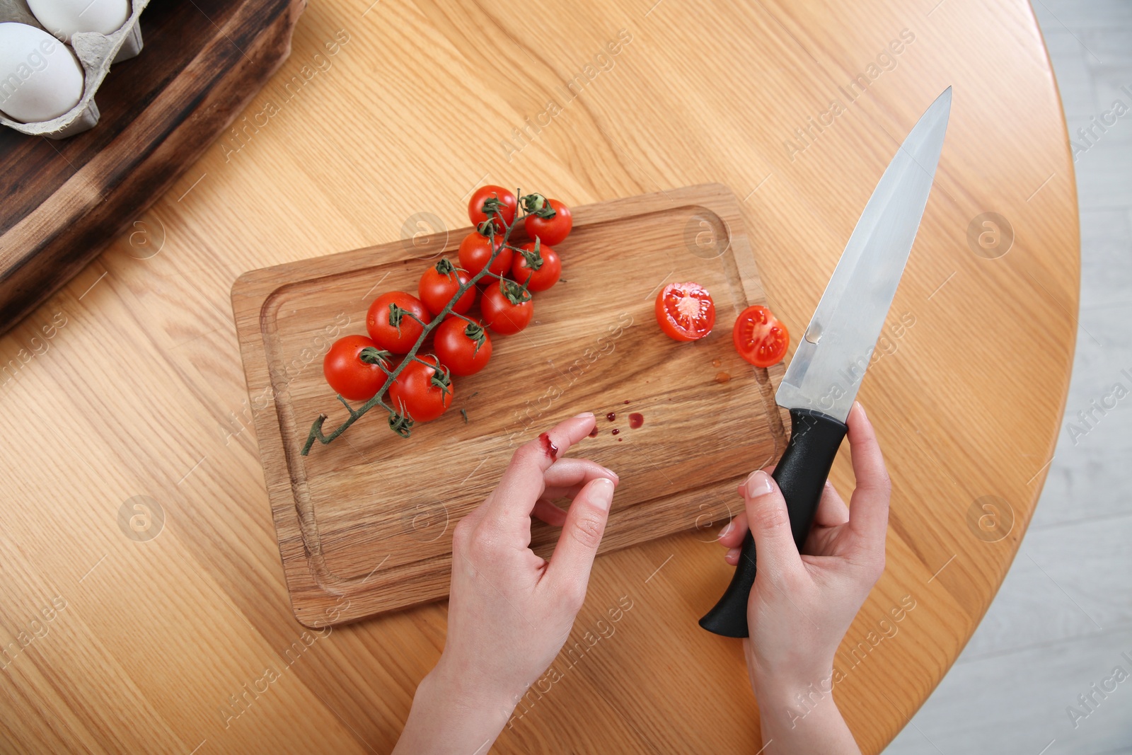 Photo of Woman cut finger with knife while cooking at wooden table, closeup, top view