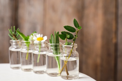 Photo of Glass bottles of different essential oils with plants on table