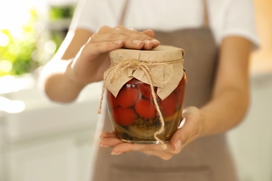 Woman holding jar of pickled tomatoes indoors, closeup