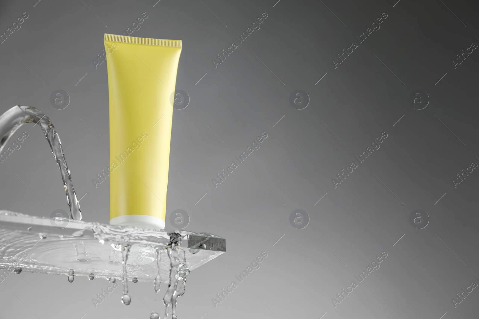 Photo of Moisturizing cream in tube on glass with water drops against grey background, low angle view. Space for text
