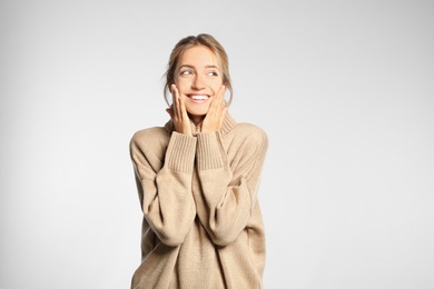 Beautiful young woman wearing knitted sweater on light grey background