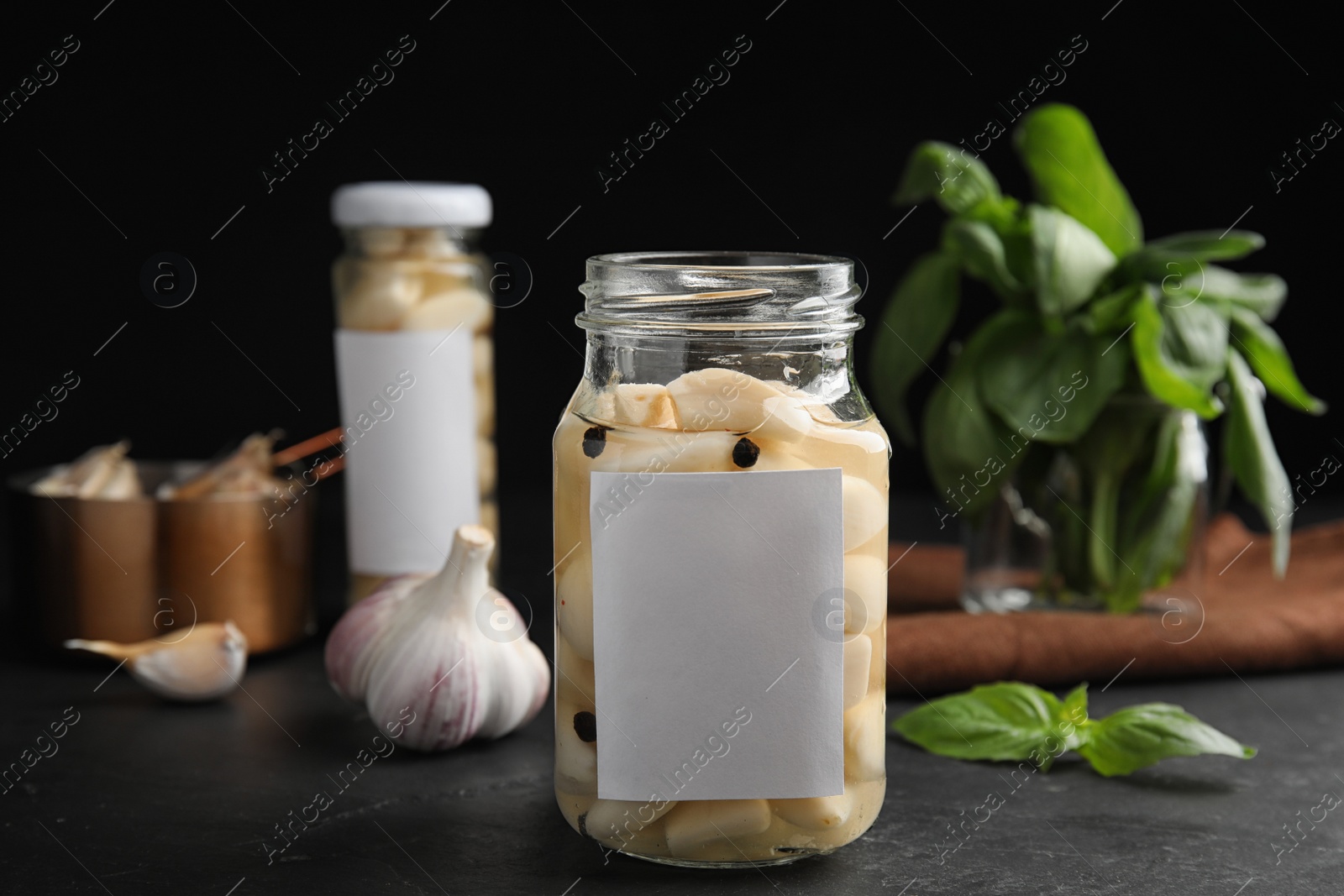 Photo of Composition with jar of pickled garlic on dark table against black background