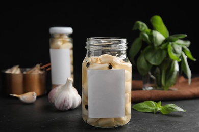 Composition with jar of pickled garlic on dark table against black background