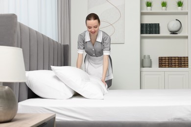 Photo of Young maid making bed in hotel room