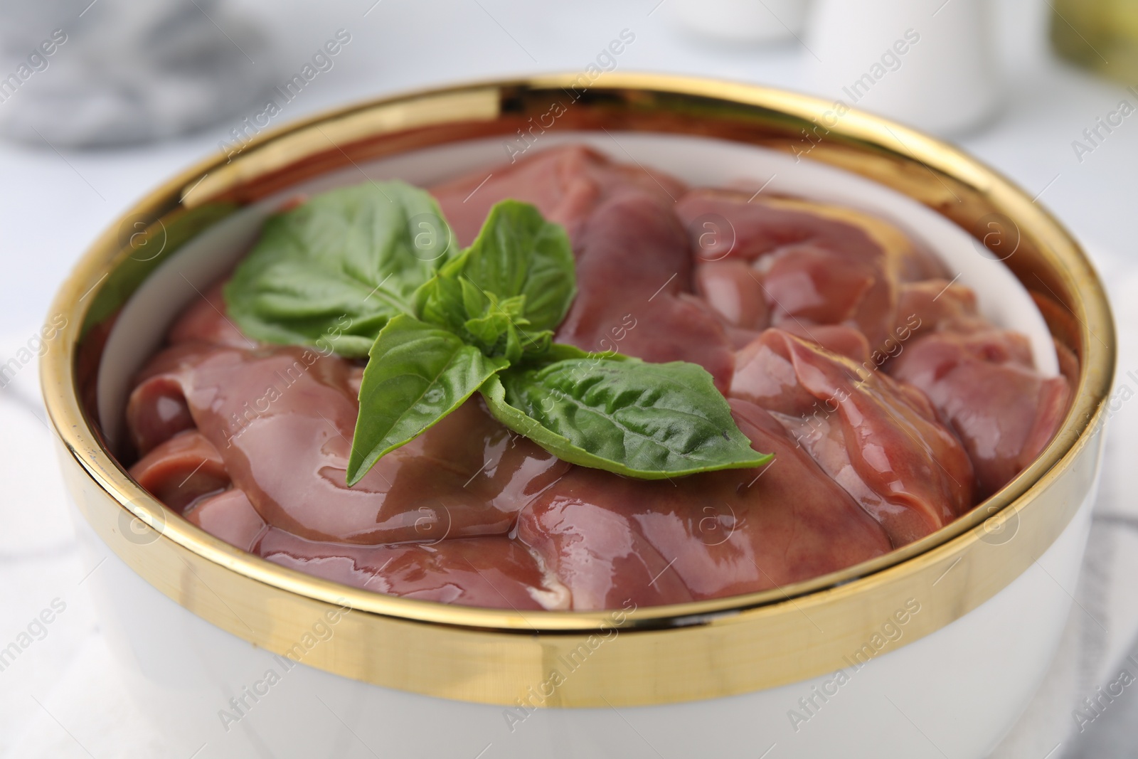 Photo of Bowl with raw chicken liver and basil on table, closeup